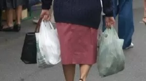Donna anziana di spalle che trasporta buste della spesa